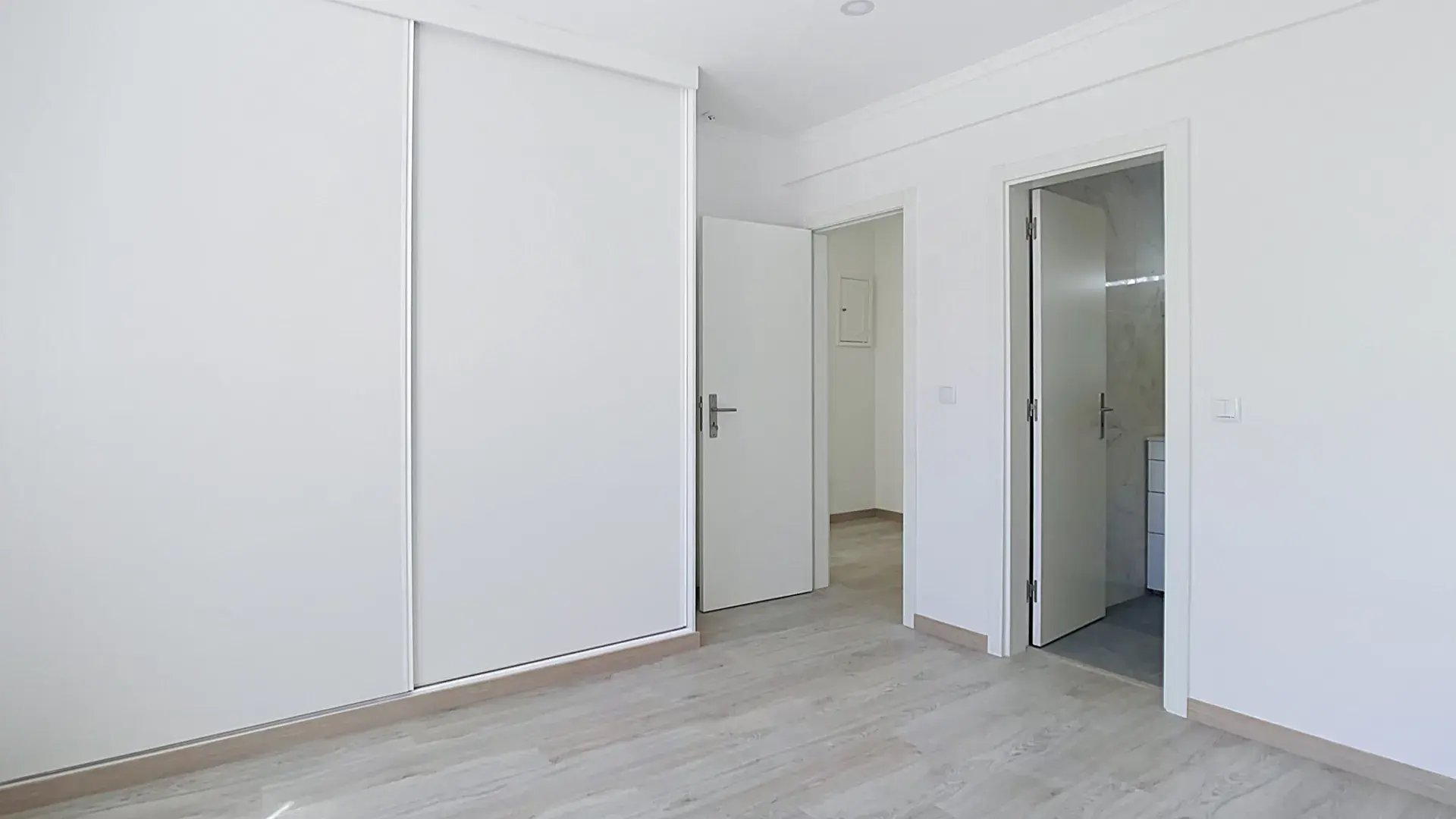 Suite bedroom with floor-to-ceiling wardrobe and ensuite bathroom doorway in Massamá