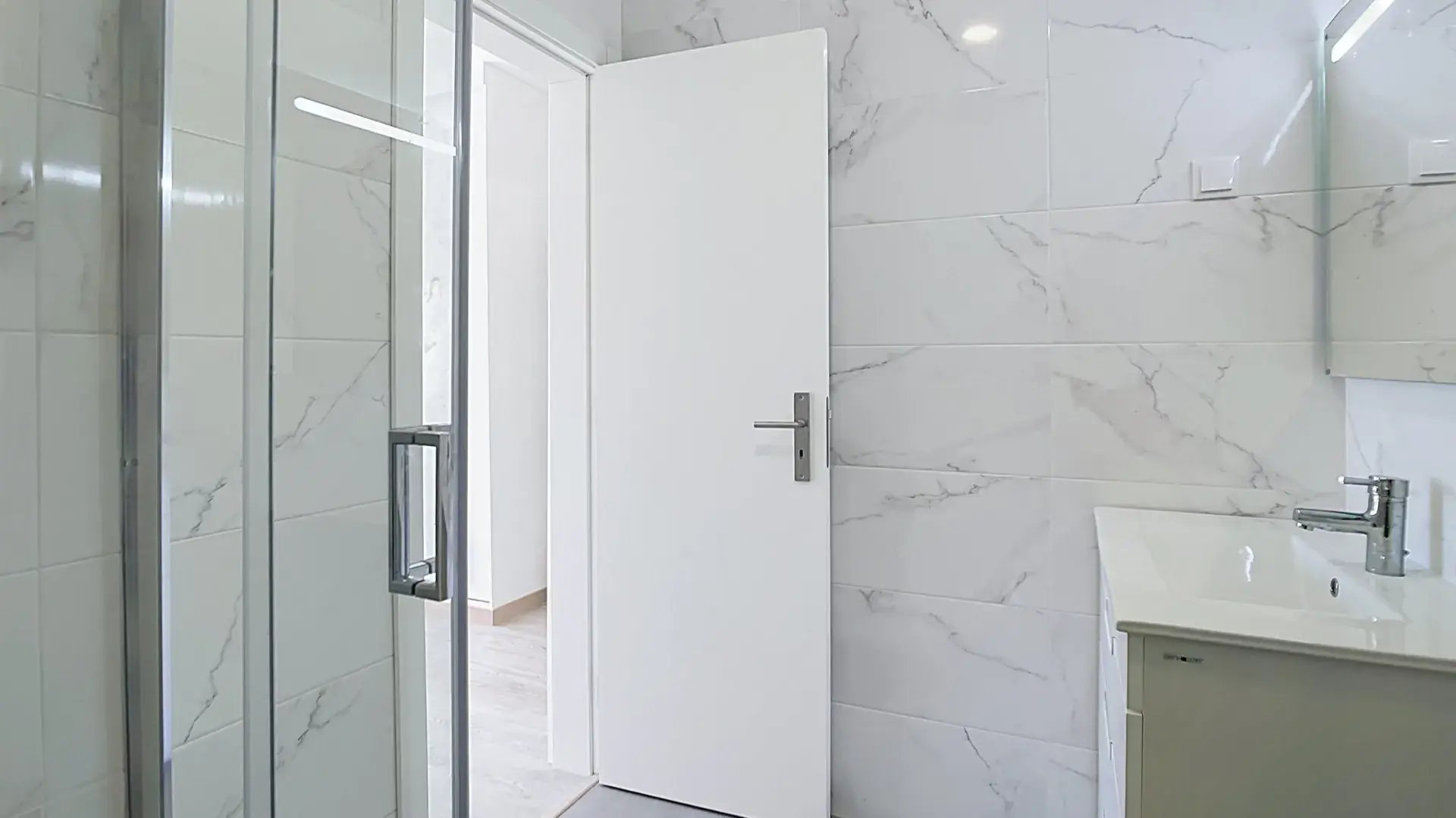 Renovated bathroom with glass shower enclosure and marble-effect wall tiles in Massamá