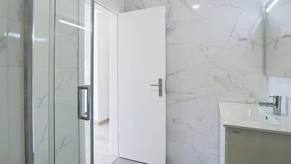 Renovated bathroom with glass shower enclosure and marble-effect wall tiles in Massamá