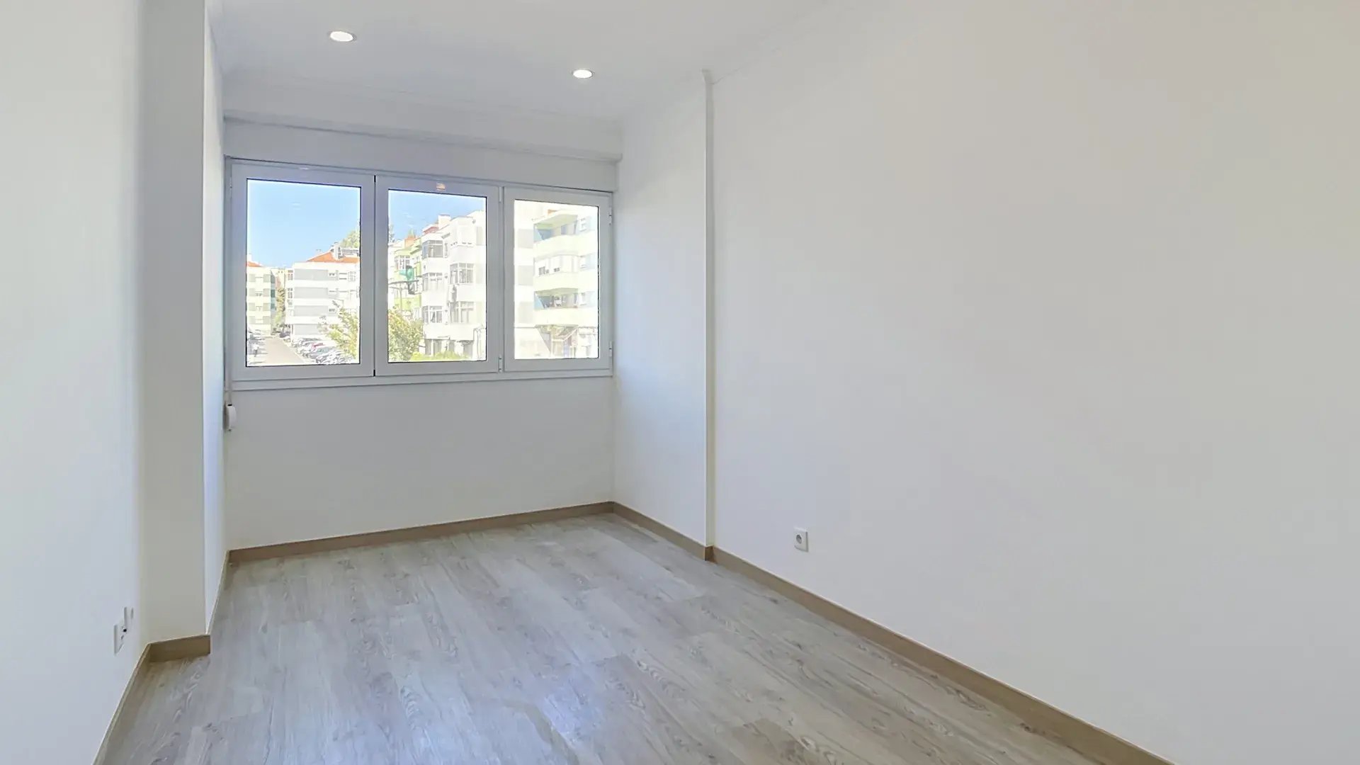 Bright empty bedroom with large window overlooking Massamá residential buildings