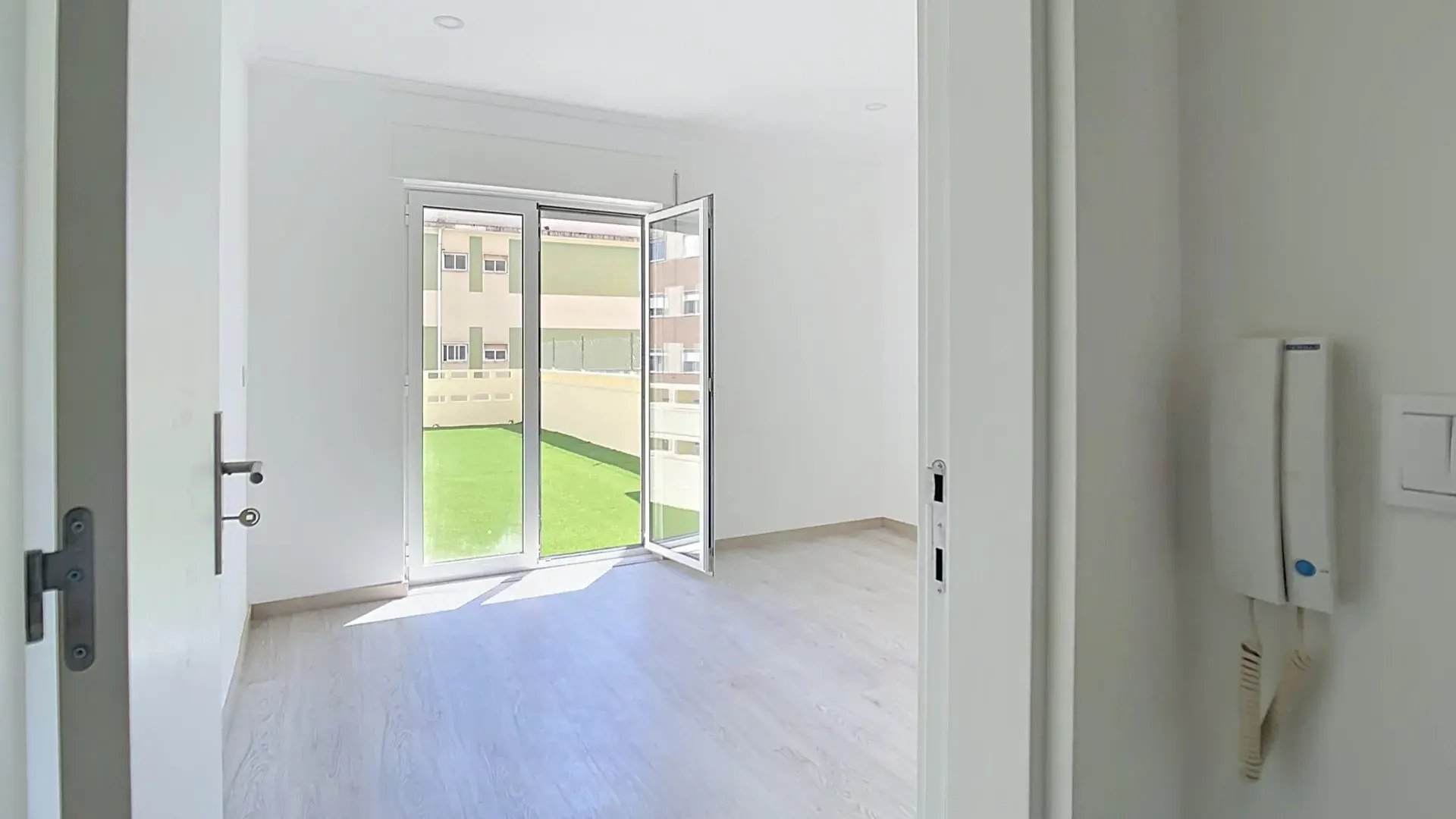 Bright room with open glass doors leading to a green terrace in the Massamá T3