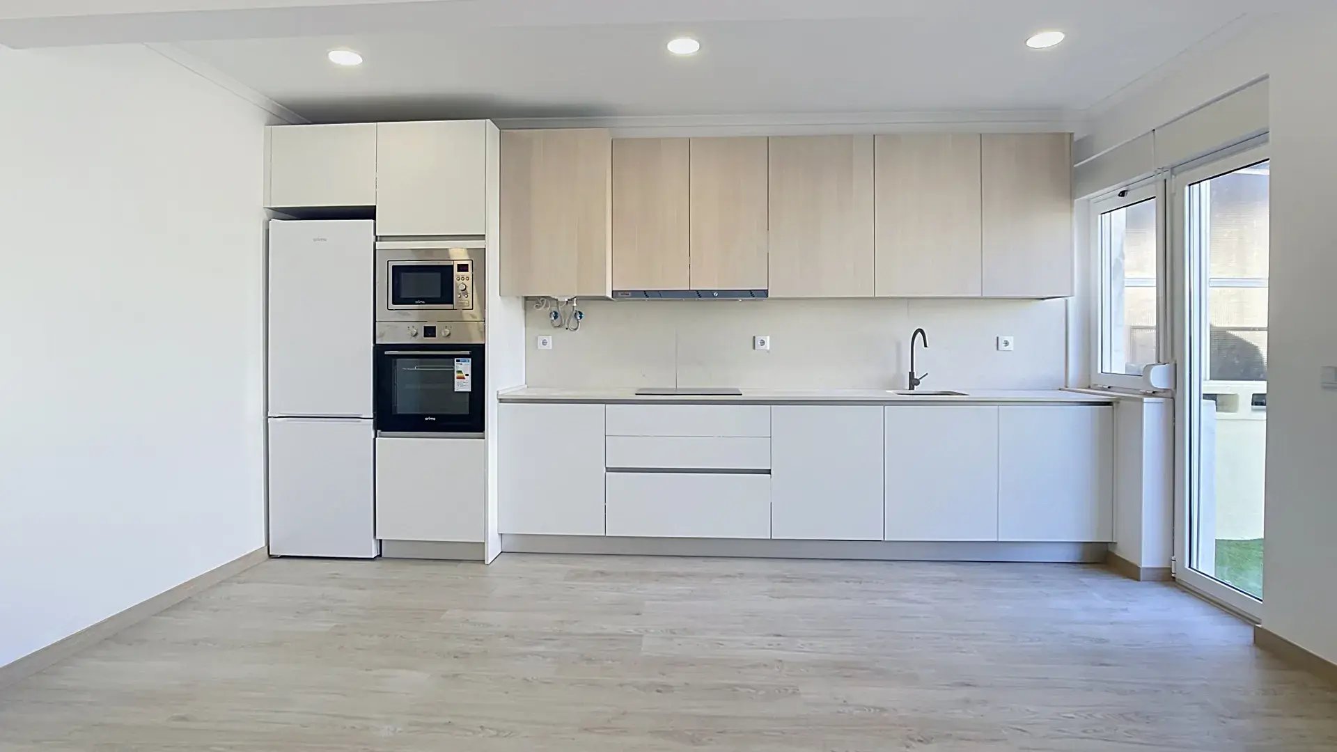 Contemporary kitchen with wood wall cabinets, white base units and black faucet in a Massamá T3