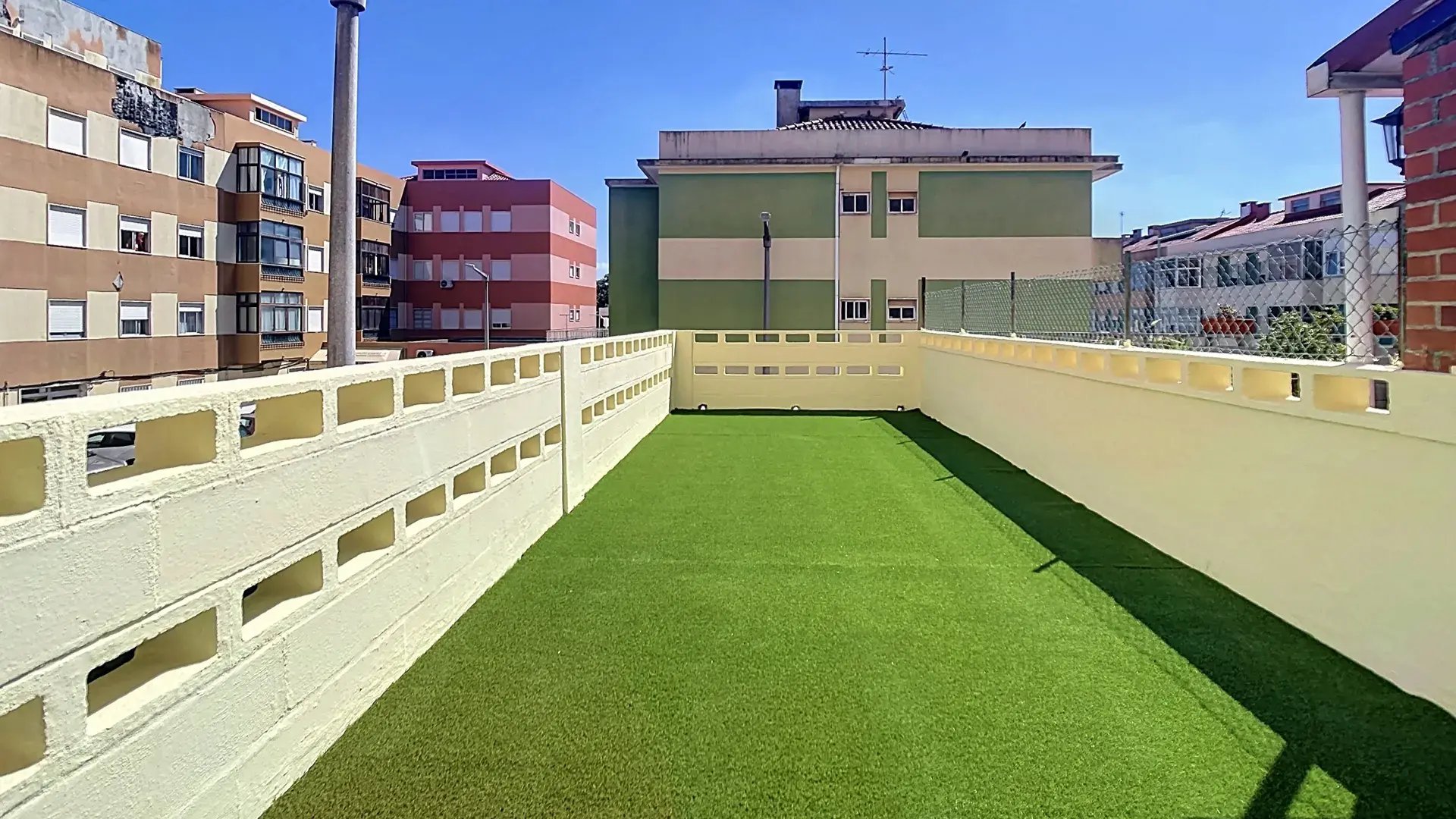 Long private terrace with artificial turf overlooking residential Massamá on a sunny day