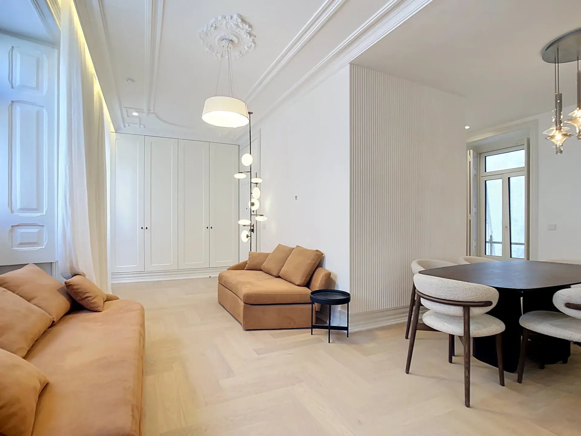 Bright open-plan living room of a 3-bedroom apartment in Almirante Tridente, Lisbon, with camel sofas, herringbone wood floors and classical ceiling moldings