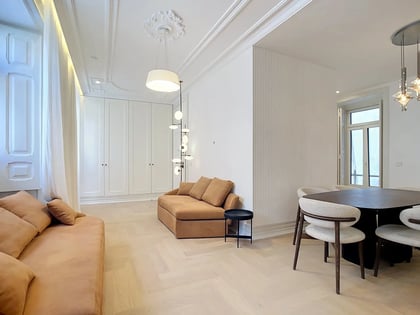 Bright open-plan living room of a 3-bedroom apartment in Almirante Tridente, Lisbon, with camel sofas, herringbone wood floors and classical ceiling moldings