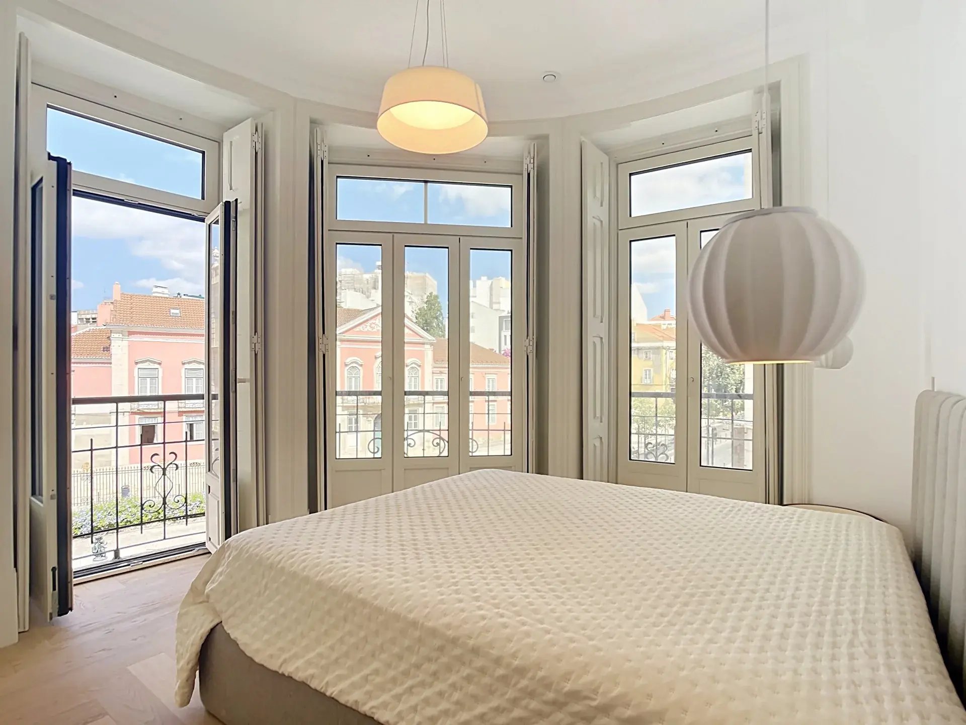 Master bedroom with curved façade and French doors opening to wrought-iron balconies overlooking Lisbon