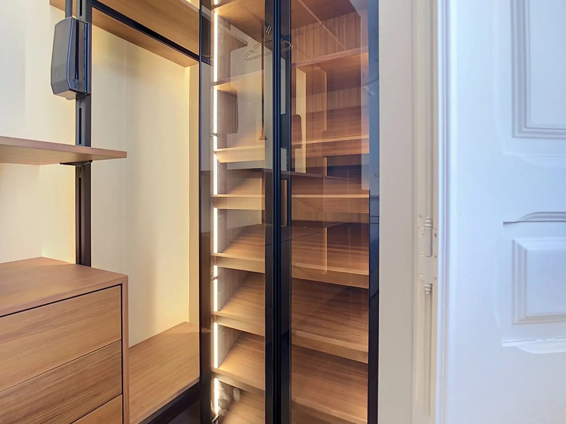 Walk-in closet with warm wood shelving, smoked glass doors and integrated LED lighting