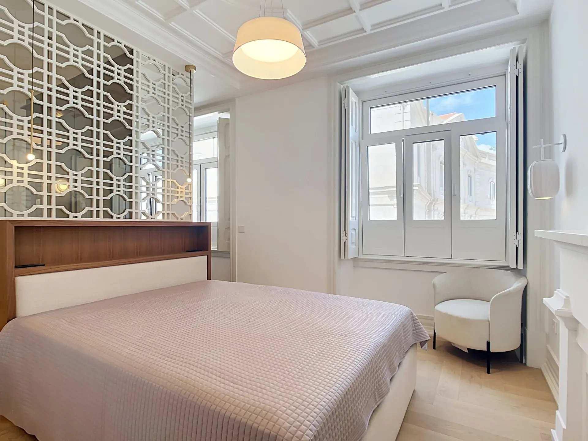Second bedroom with geometric lattice headboard wall and large shuttered window in a Lisbon T3 apartment