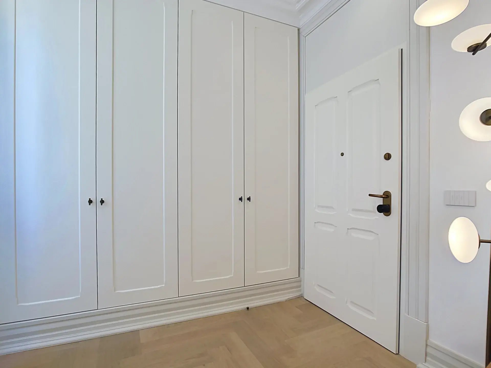 Bright entrance hall with floor-to-ceiling white wardrobes and herringbone wood flooring