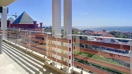 South-facing terrace with metal railing and a sea view over red rooftops in Parede