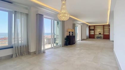 Living room of a top-floor penthouse in Parede, Cascais, with stone floors and windows opening onto the Atlantic