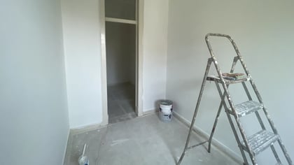 Bedroom under renovation with floor protection, stepladder, and bright window.