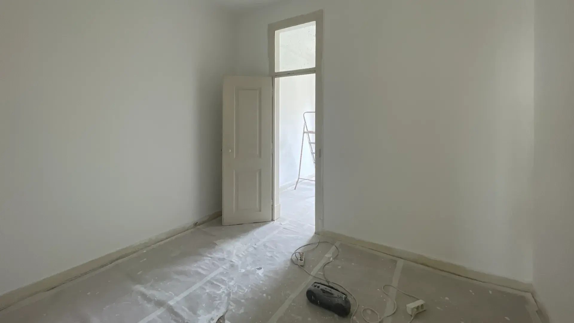 Kitchen under renovation with tools, paint buckets, white cabinets, and tiled walls.