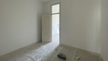 Kitchen under renovation with tools, paint buckets, white cabinets, and tiled walls.