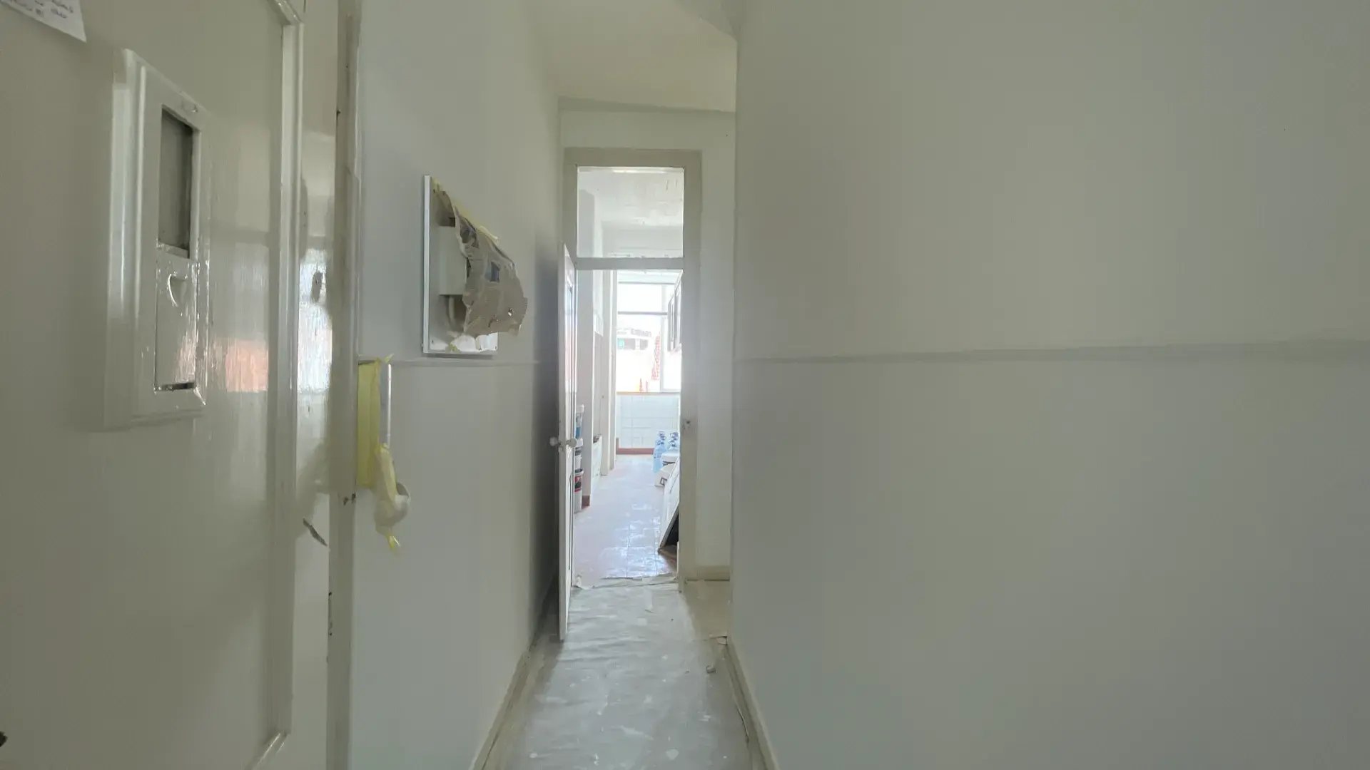 Bright empty hallway with white walls, light wood floors, and natural light from an open doorway.