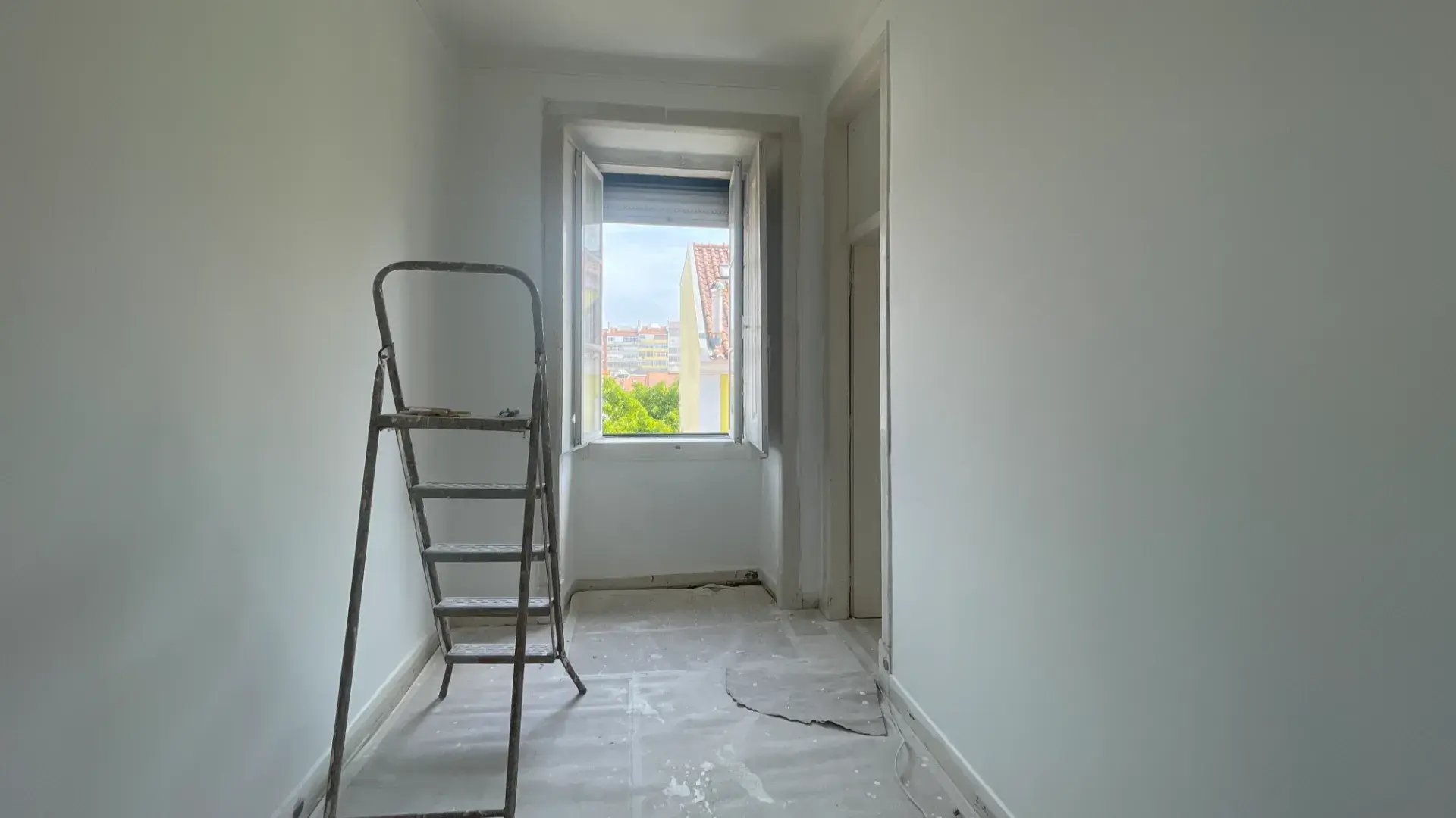 Empty bright room with light wood floors and open door leading to a sunlit hallway.