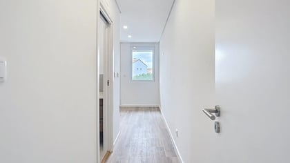 Corredor interior luminoso com pavimento em madeira, paredes brancas imaculadas e várias portas de acesso.