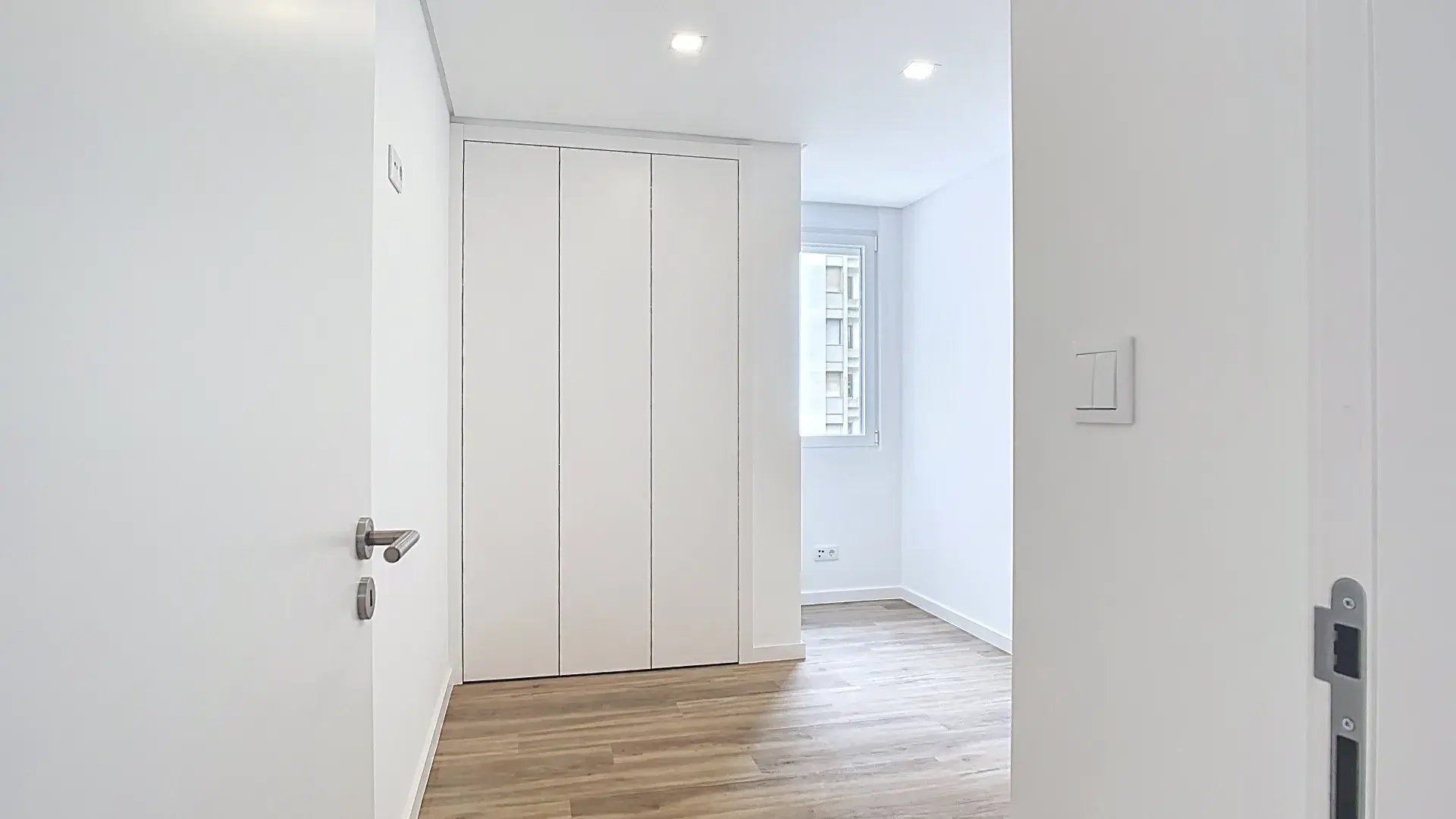 Roupeiro embutido de portas brancas fechadas num quarto moderno e bem iluminado com pavimento flutuante.