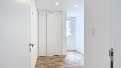 Roupeiro embutido de portas brancas fechadas num quarto moderno e bem iluminado com pavimento flutuante.