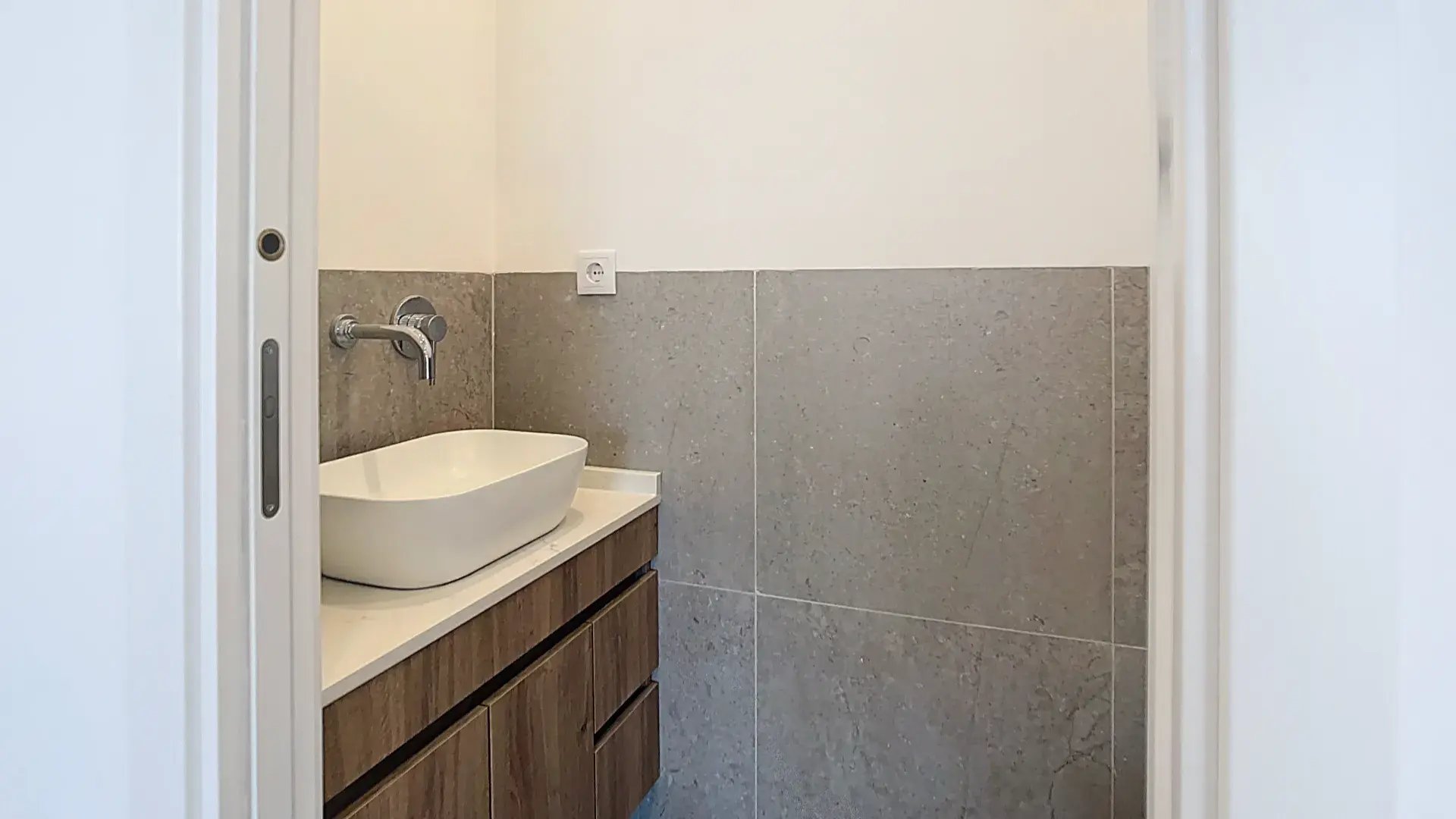 Casa de banho moderna com lavatório branco pousado sobre um móvel suspenso e torneira cromada de parede.