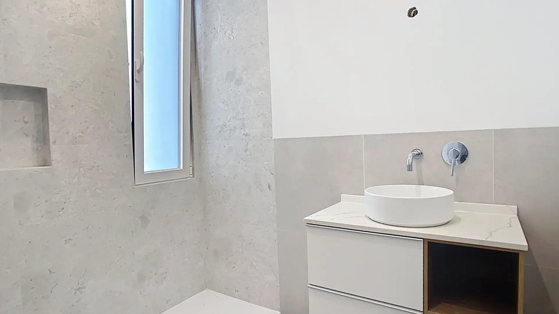 Casa de banho moderna com lavatório branco pousado sobre um móvel suspenso e torneira cromada de parede.