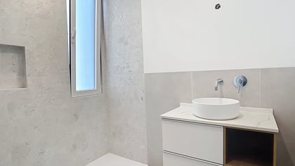 Casa de banho moderna com lavatório branco pousado sobre um móvel suspenso e torneira cromada de parede.