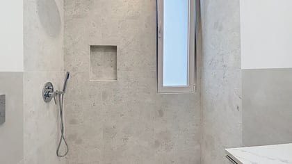 Área de duche moderna com revestimento em pedra cinzenta, nicho embutido na parede e sistema de chuveiro cromado.