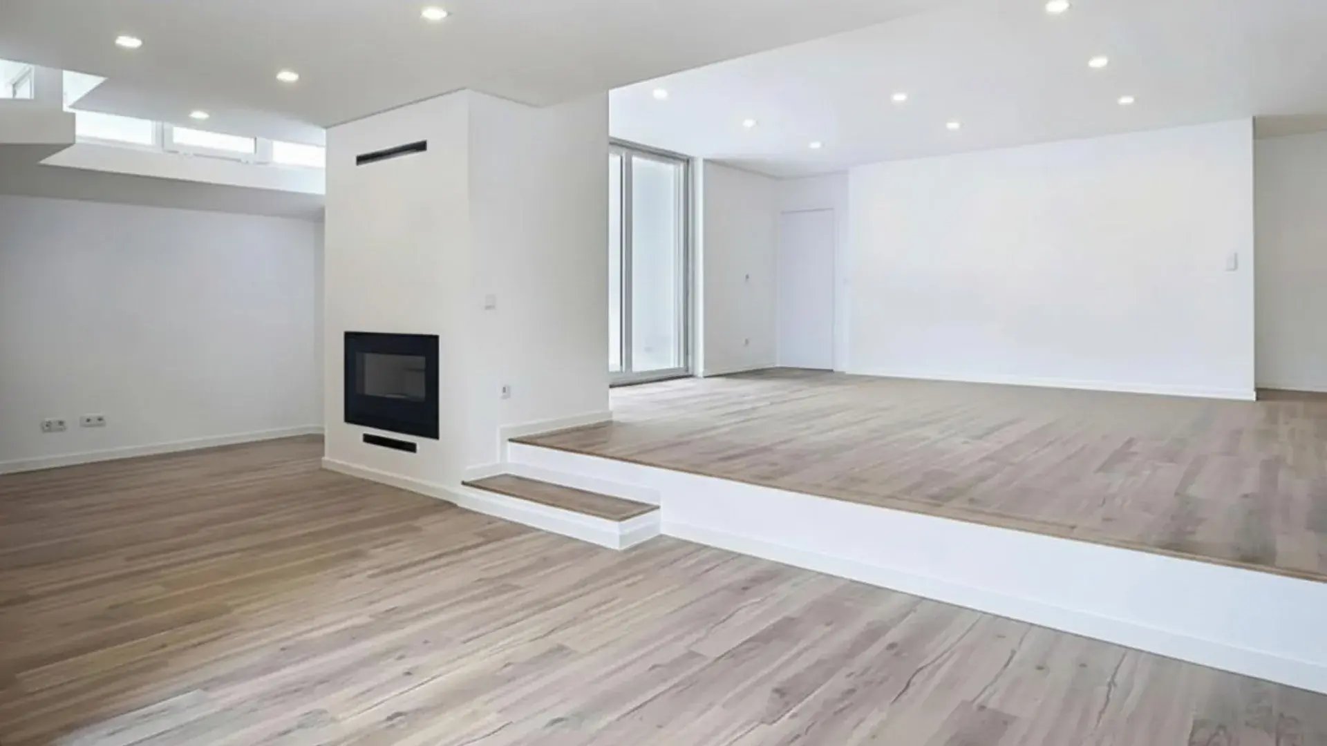 Sala de estar ampla e luminosa com pavimento em madeira clara, zona de estar em desnível e uma lareira moderna embutida.