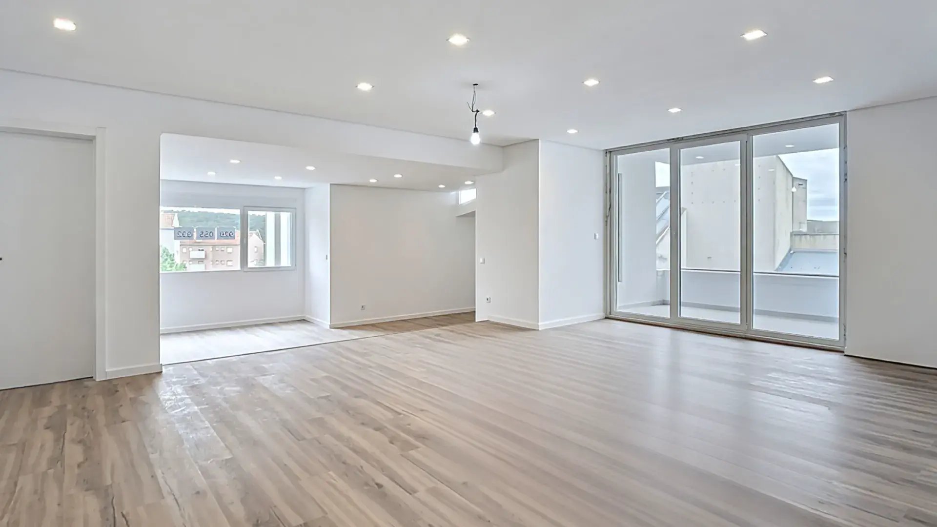 Sala de estar espaçosa e vazia com focos de luz e grandes portadas de vidro com acesso à varanda.