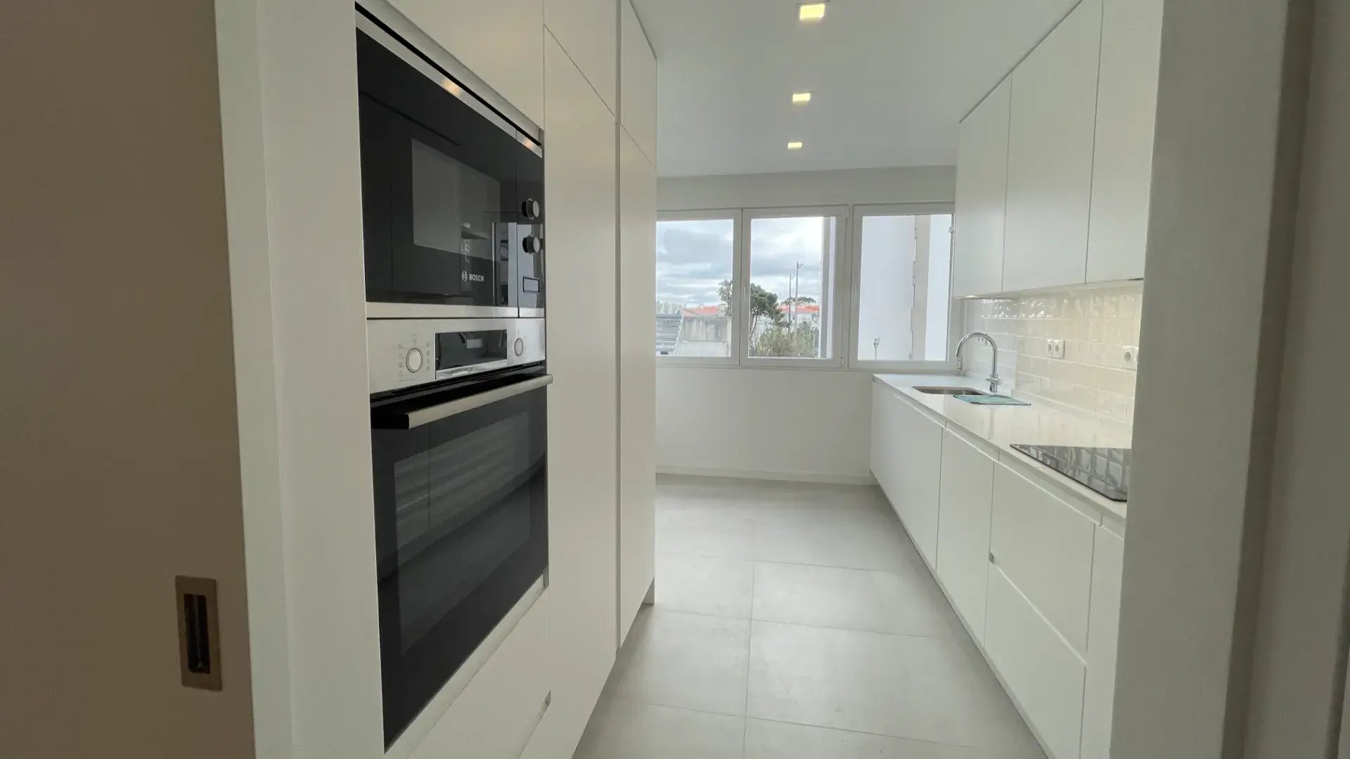Cozinha moderna linear com armários brancos, forno e microondas embutidos da marca Bosch.