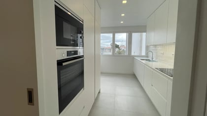Cozinha moderna linear com armários brancos, forno e microondas embutidos da marca Bosch.