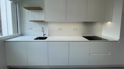 Bancada de cozinha em quartzo branco com placa de indução preta, lava-louça embutido e prateleiras de madeira.