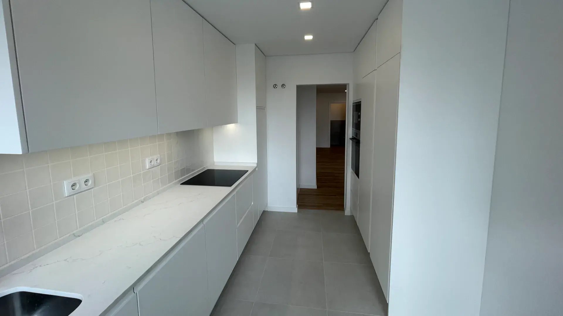 Vista geral do corredor da cozinha moderna em tons brancos com iluminação LED no teto.