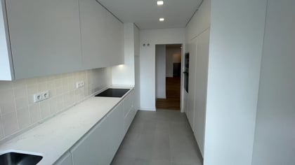 Vista geral do corredor da cozinha moderna em tons brancos com iluminação LED no teto.